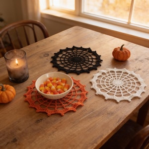 a wooden table with a bowl of candy, a candle, and two crocheted place mats, one orange and one white, along with a small pumpkin and a spider web doily.