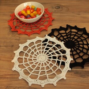 a wooden table with three crocheted place mats, a bowl of candy, and a green ceramic object.