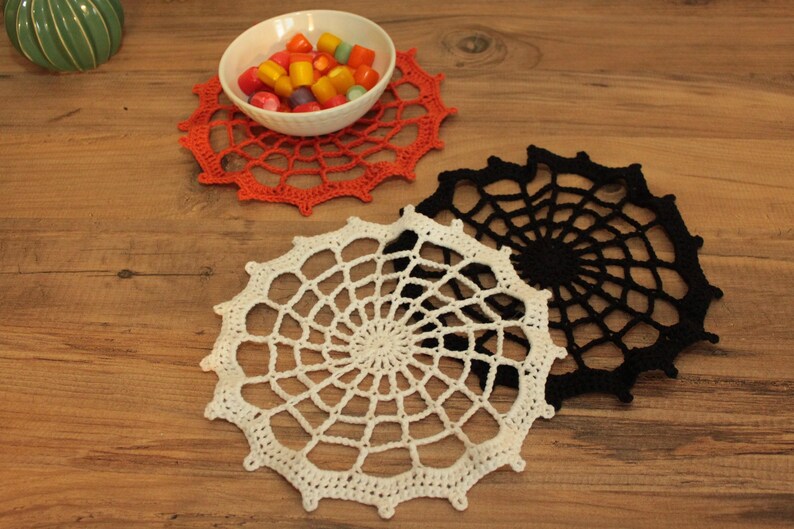 a wooden table with three crocheted place mats, a bowl of candy, and a green ceramic object.
