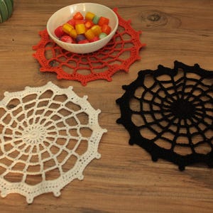 a wooden table with three crocheted doily pieces, a bowl of candy, and a small green plant.