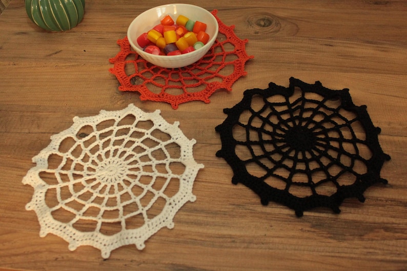a wooden table with three crocheted doily pieces, a bowl of candy, and a small green plant.