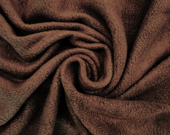 May include: Close-up of a brown, soft, and textured fabric. The fabric is folded and twisted, creating a swirling pattern.