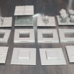 May include: A set of 10 gray, square, miniature tiles with various designs. Some tiles have a textured surface, while others have a smooth surface with a square cutout in the center.