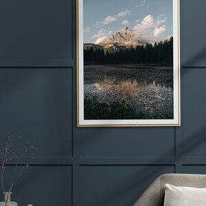 Può includere: Una fotografia incorniciata di una montagna riflessa in un lago tranquillo. La montagna è di colore marrone chiaro ed è ricoperta di alberi verdi. Il lago è di colore blu scuro e il cielo è di colore blu chiaro con nuvole bianche.