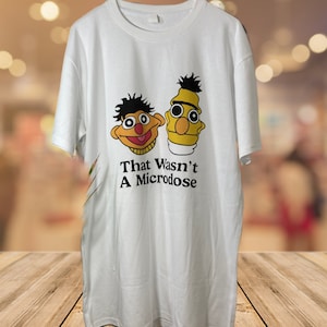 Peut inclure: T-shirt blanc avec un motif de Bert et Ernie de Sesame Street. Le texte "That Wasn't A Microdose" est imprimé sous les personnages.