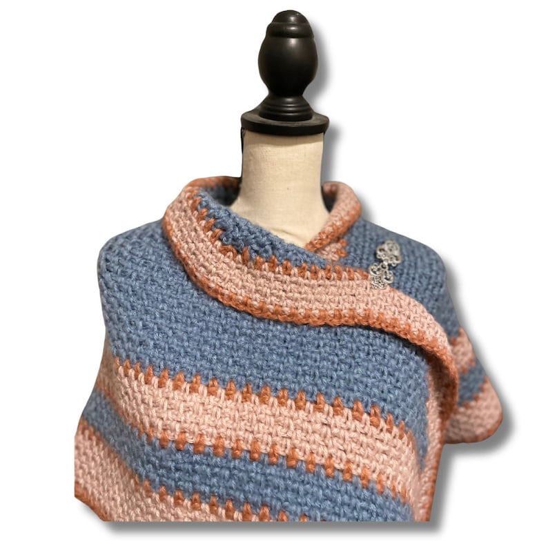 May include: A blue and pink striped crocheted shawl draped over a mannequin. The shawl has a decorative crocheted border.