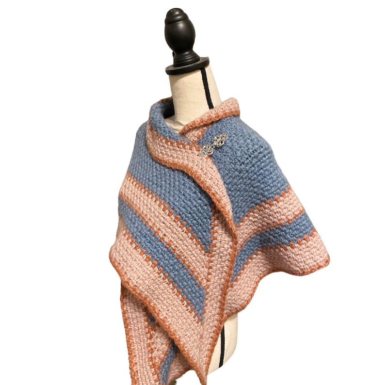 May include: A blue and peach striped crocheted shawl with a decorative pin.