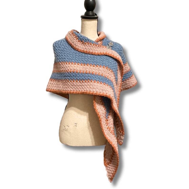 May include: A blue and pink striped crocheted shawl with a decorative pin.