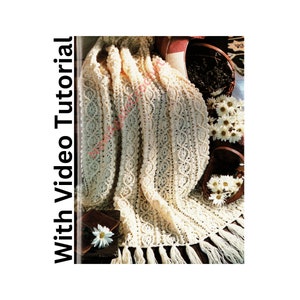 Può includere: Una coperta all'uncinetto con un delicato motivo a pizzo di colore crema. La coperta ha un bordo a frangia ed è drappeggiata su un cesto di fiori.