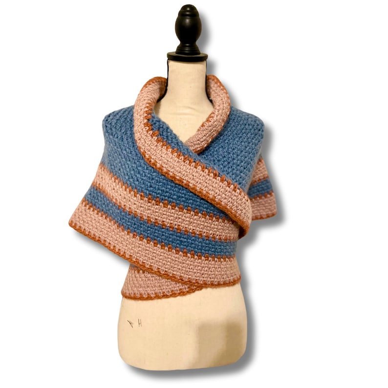 May include: A blue and pink striped crocheted shawl draped over a white mannequin. The shawl is made with a soft, textured yarn and has a simple, elegant design.