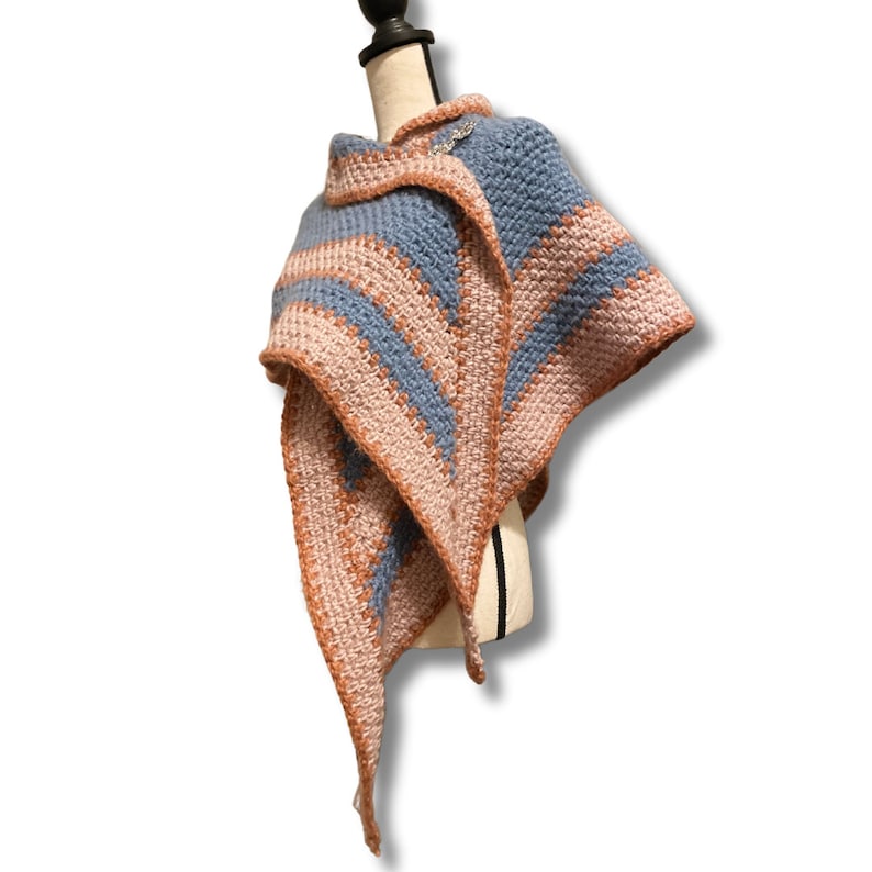 May include: A blue and pink crocheted shawl with a decorative pin. The shawl is draped over a dress form.