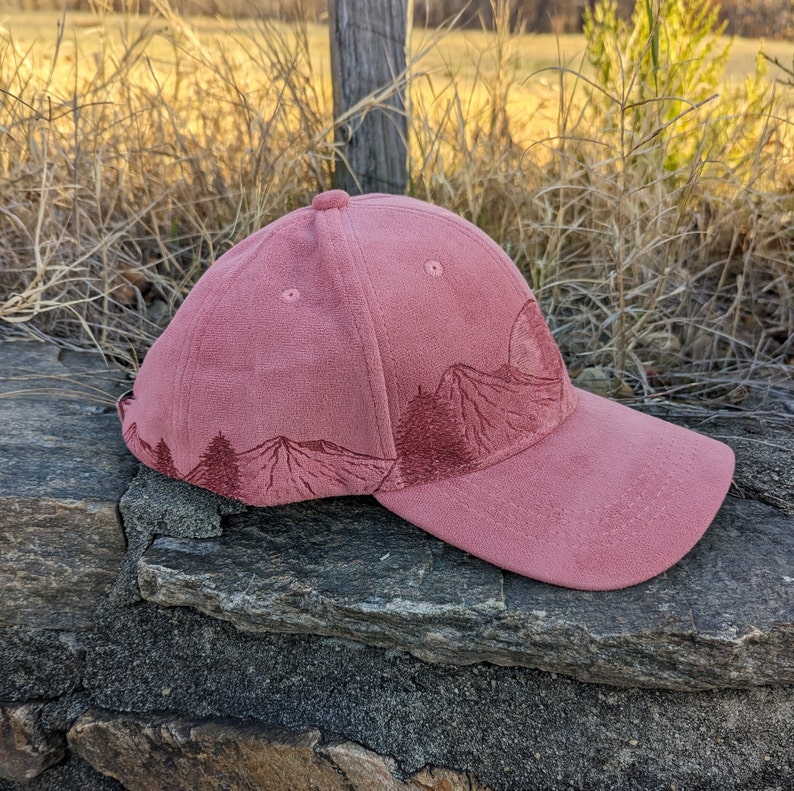 May include: A pink corduroy baseball cap with an embroidered mountain scene. The cap has a curved brim and a relaxed fit.