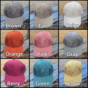 May include: Nine different colored baseball caps with an embroidered mountain scene and birds in flight. The colors are brown, tan, beige, orange, pink, gray, berry, green, and yellow.