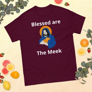 Könnte beinhalten: Burgunderfarbenes T-Shirt mit einer weißen Grafik von Jesus, der ein Lamm hält. Der Text "Blessed are The Meek" ist in Weiß unter dem Bild gedruckt.