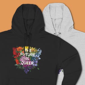 May include: Two hooded sweatshirts, one black and one gray, are displayed. The black sweatshirt features a floral design in rainbow colors with the text "THE FUTURE IS QUEER" in white. Both sweatshirts have a front pocket and a hood.