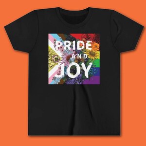May include: Black t-shirt featuring a floral design with the words "Pride and Joy" in white. The floral arrangement incorporates colors from various pride flags, including the transgender flag, rainbow flag, and others.