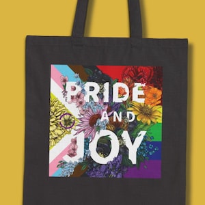 May include: Black tote bag with a colorful floral design and the text "PRIDE AND JOY". The flowers are arranged in a rainbow pattern, representing the LGBTQ+ pride flag.