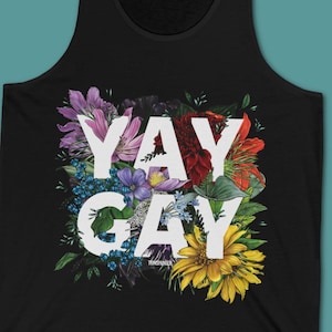 May include: A black tank top featuring a large white graphic with the text YAY GAY. The text is surrounded by a colourful illustration of various flowers including purple, red, and yellow blossoms, along with green leaves and small blue berries.