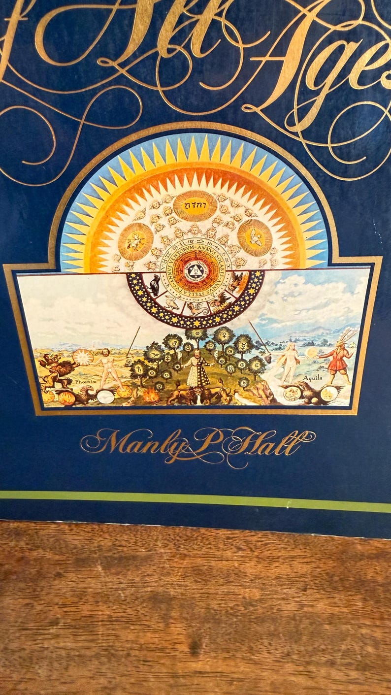 Może przedstawiać: Ciemnoniebieski nadruk ze złotymi literami i szczeg&oacute;łowymi ilustracjami. Grafika zawiera obrazy niebieskie i symboliczne, z nazwiskiem "Manly P. Hall" na dole. Na g&oacute;rze nadruku widnieją złote słowa "All Ages".