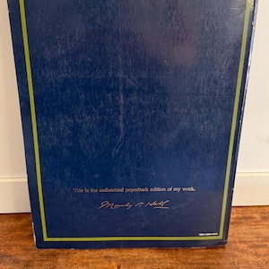 Może przedstawiać: Ciemnoniebieska książka w miękkiej oprawie ze złotą obw&oacute;dką. Na okładce znajduje się napis "This is the authorized paperback edition of my work" oraz podpis. Dzieło literackie.