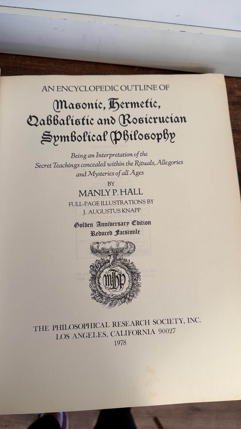 Może przedstawiać: Otwarta książka zatytułowana "An Encyclopedic Outline of Masonic, Hermetic, Qabbalistic and Rosicrucian Symbolical Philosophy" autorstwa Manly'ego P. Halla. Złote wydanie rocznicowe, opublikowane w 1978 roku przez The Philosophical Research Society, Inc.