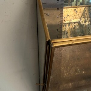 May include: A rectangular, brass-toned display case with mirrored glass panels. The case is approximately 7 inches long. The case has a hinged lid and a small latch. The case is empty.