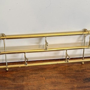 May include: A vintage brass wall-mounted coat rack with two horizontal bars and multiple hooks. The brass has a warm, golden hue, and the design is simple yet functional. Perfect for entryways or bedrooms.