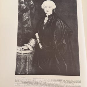 Może przedstawiać: Czarno-biały portret mężczyzny w ciemnym płaszczu i peruce, trzymającego zw&oacute;j. Obraz pochodzi z książki, z tekstem na dole. Herb jest widoczny w prawym g&oacute;rnym rogu. Portret jest historycznym przedstawieniem.