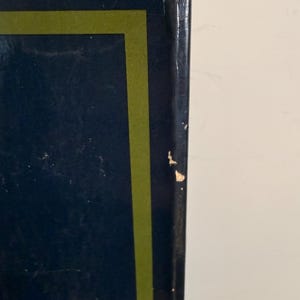 Może przedstawiać: Zbliżenie grzbietu książki. Grzbiet jest granatowy z zieloną obw&oacute;dką. G&oacute;rna krawędź książki nosi ślady zużycia. Książka jest na białym tle.