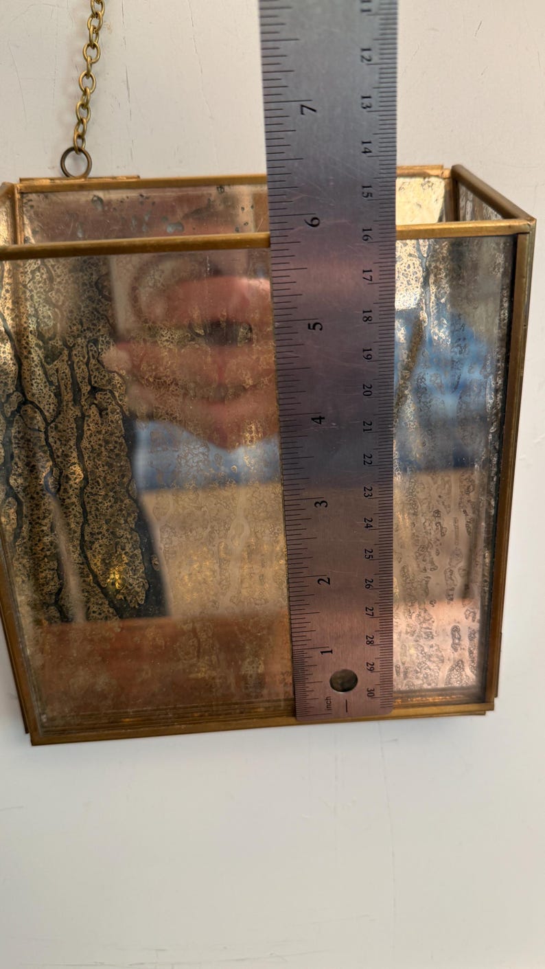 May include: A rectangular, vintage-style hanging planter with a tarnished brass frame and mirrored glass. The planter is approximately 6 inches tall. A brass chain is attached for hanging. The glass has a distressed, antique appearance.