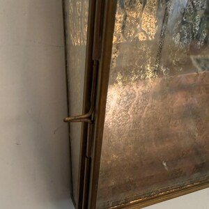 May include: A rectangular, antique-style display case with a tarnished brass frame. The glass has a textured, mottled appearance. A latch secures the case, suggesting it opens. The case is likely for displaying small items.