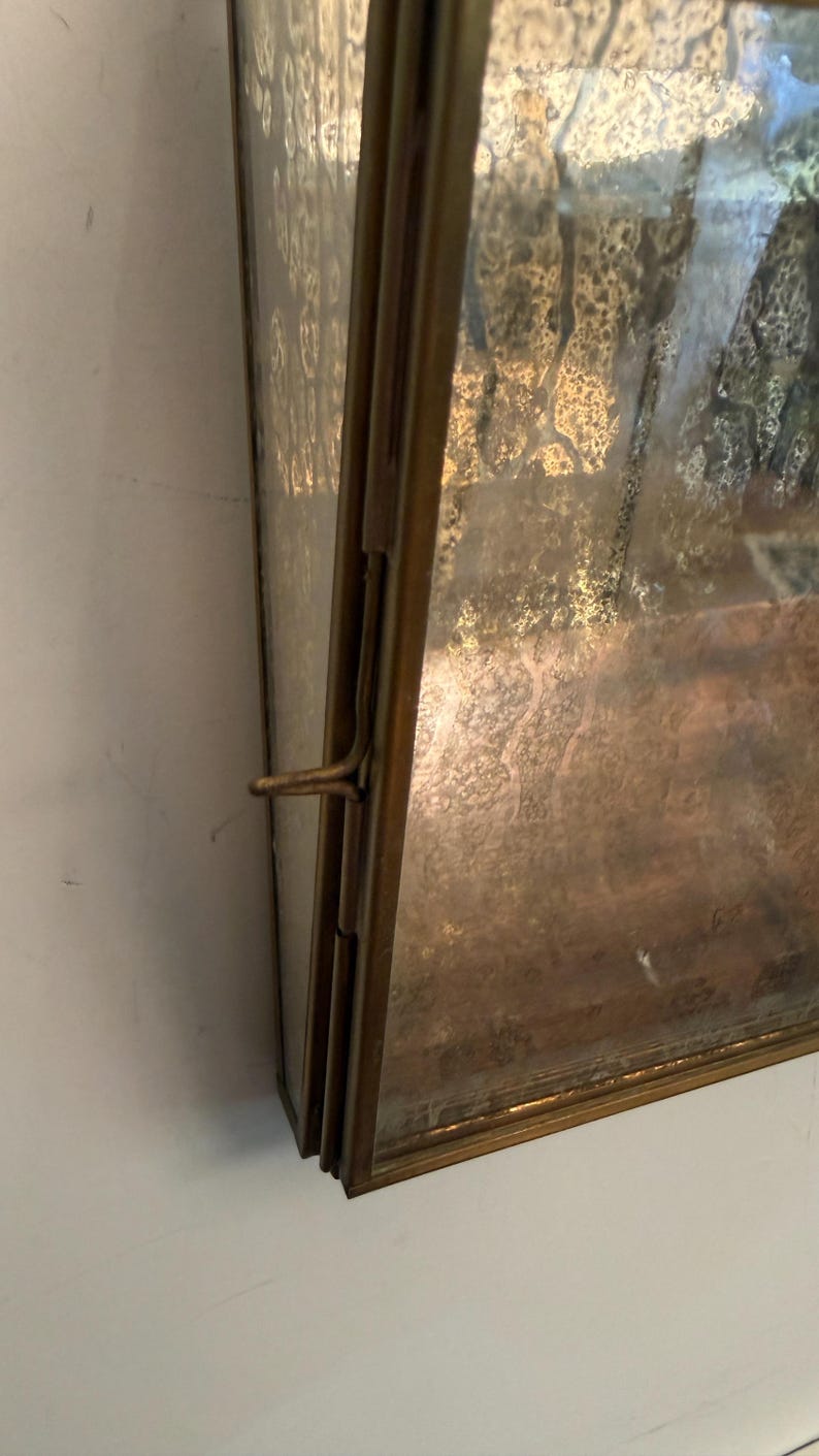 May include: A rectangular, antique-style display case with a tarnished brass frame. The glass has a textured, mottled appearance. A latch secures the case, suggesting it opens. The case is likely for displaying small items.