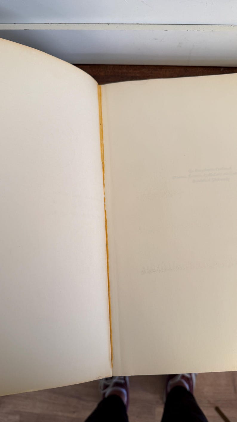 Może przedstawiać: Otwarta książka z postarzanymi, kremowymi stronami. Krawędź oprawy ma złoty brązowy kolor. Strony są puste, z bladym tekstem widocznym na prawej stronie. Książka jest otwarta, ukazując wewnętrzne strony.