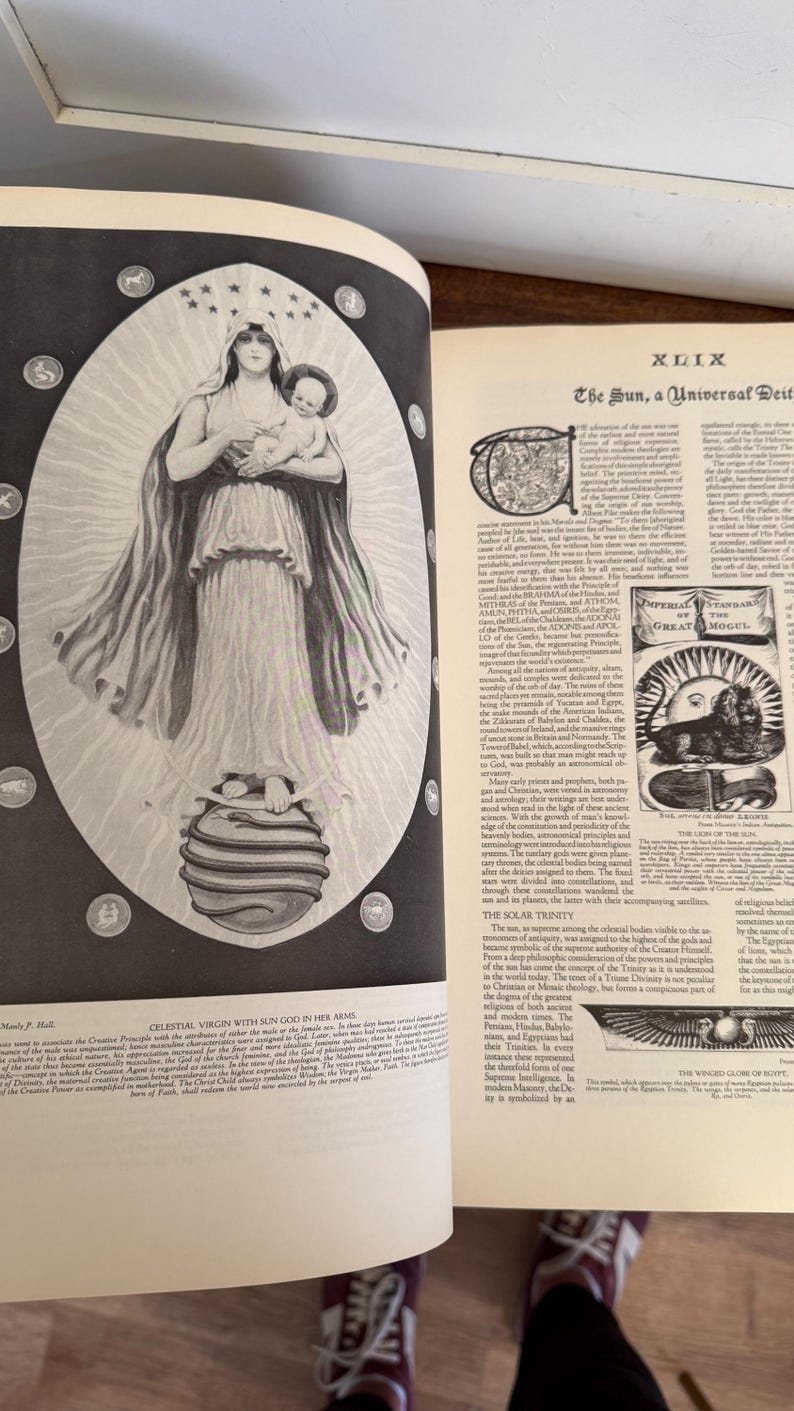 Może przedstawiać: Czarno-biała ilustracja z książki przedstawiająca niebiańską dziewicę trzymającą dziecko, stojącą na globie. Obraz otoczony jest okrągłymi wzorami i tekstem. Tekst brzmi "Celestial Virgin with Sun God in Her Arms."