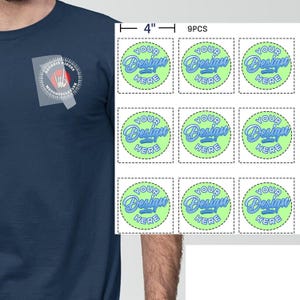 Puede incluir: Camiseta azul marino con el logo del Detroit Riders Motorcycle Club. Nueve pegatinas circulares, cada una de 10 cm de diámetro, con el texto "YOUR Design HERE" en azul sobre fondo verde.
