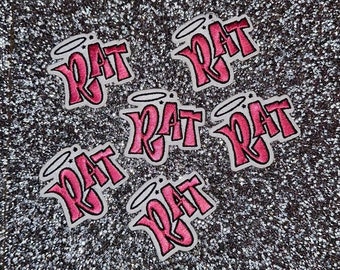 以下が含まれることがあります： グラフィティスタイルのフォントで「RAT」と書かれたピンクのアイロン接着パッチが6つ。各パッチには、単語の上にハローがあります。