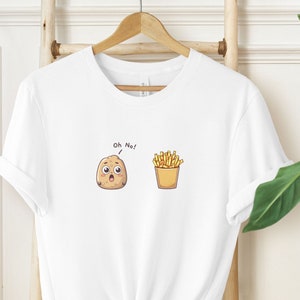 Puede incluir: Camiseta blanca con un gráfico de dibujos animados de una patata y patatas fritas. La patata tiene una expresión de sorpresa y dice "¡Oh, no!"