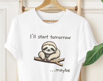 Könnte beinhalten: Weißes T-Shirt mit einem Cartoon-Faultier auf einem Ast und dem Text "I'll start tomorrow...maybe". Das Faultier ist hellbraun und der Ast ist braun. Das T-Shirt hängt an einem Holzbügel.