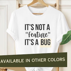 May include: White t-shirt with the text "It's not a "feature" it's a bug" printed on the front. The text is in black. The t-shirt is available in other colours.