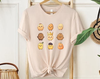 May include: A light beige t-shirt with a graphic print of nine cartoon potatoes with different expressions and accessories. The potatoes are arranged in a grid pattern on the shirt.