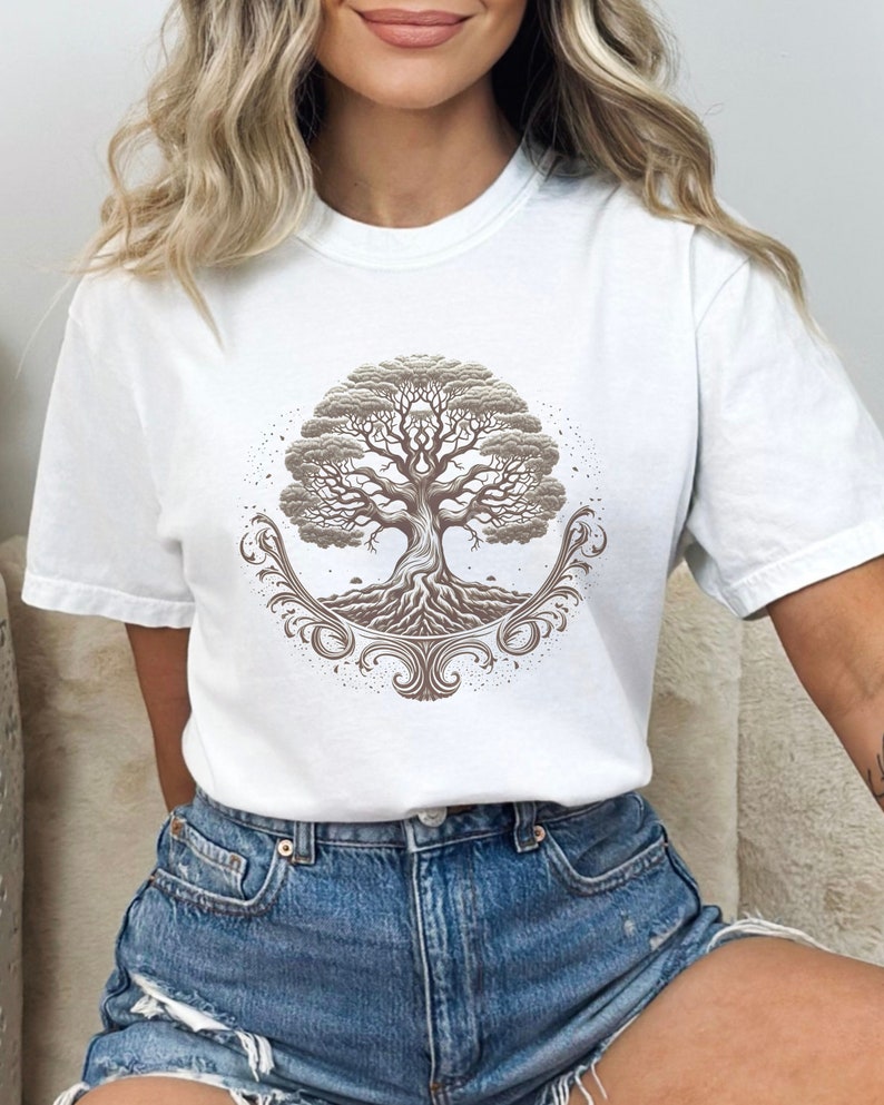 May include: White t-shirt with a brown tree of life design. The tree has intricate roots and branches, and is surrounded by a decorative border.