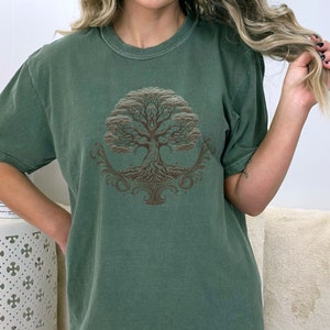 May include: A green t-shirt with a brown tree of life design. The tree has intricate roots and branches.