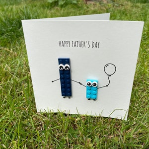 May include: A white card with the text "Happy Father's Day" and two blue Lego figures, one holding a balloon.