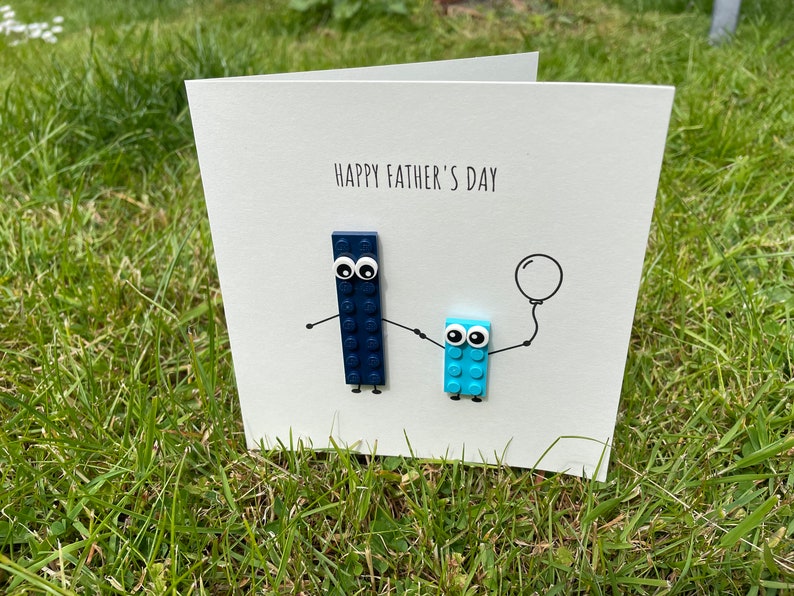 May include: A white card with the text "Happy Father's Day" and two blue Lego figures, one holding a balloon.