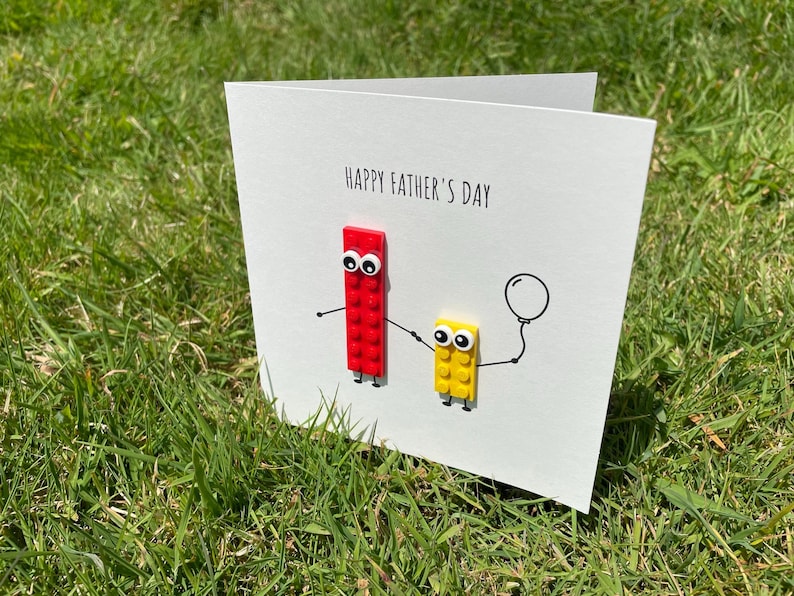 May include: A white card with the text "Happy Father's Day" and a red and yellow Lego figure holding a balloon.