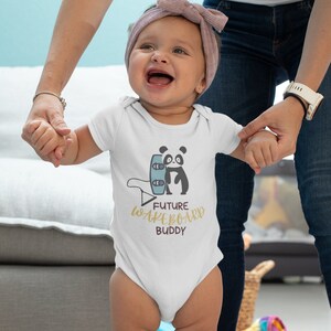 Könnte beinhalten: Weißer Baby-Strampler mit einem schwarz-weißen Panda, der ein blaues Wakeboard hält. Der Text "FUTURE WAKEBOARD BUDDY" ist in Gold auf dem Strampler gedruckt.
