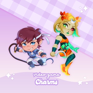 May include: Two cartoon video game charms. One is a male character in blue and white with a whip. The other is a female character in orange, green, and yellow with a crescent moon. The text "video game Charms" is at the bottom.