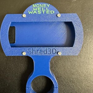 Peut inclure: Un support de t&eacute;l&eacute;phone imprim&eacute; en 3D bleu avec le texte "MONEY WELL WASTED" en haut et "Shred3D" en bas.