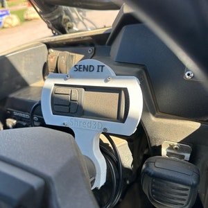 Peut inclure: Un support d'impression 3D blanc avec le texte "SEND IT" et "Shred3D" fix&eacute; au tableau de bord d'un v&eacute;hicule. Le support maintient un petit &eacute;cran num&eacute;rique avec des boutons.