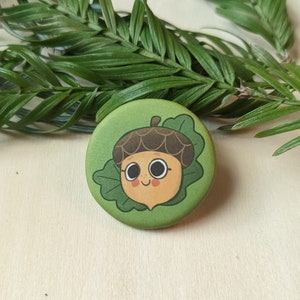 May include: A green button with a cartoon acorn wearing a brown cap and smiling. The acorn is surrounded by green leaves.